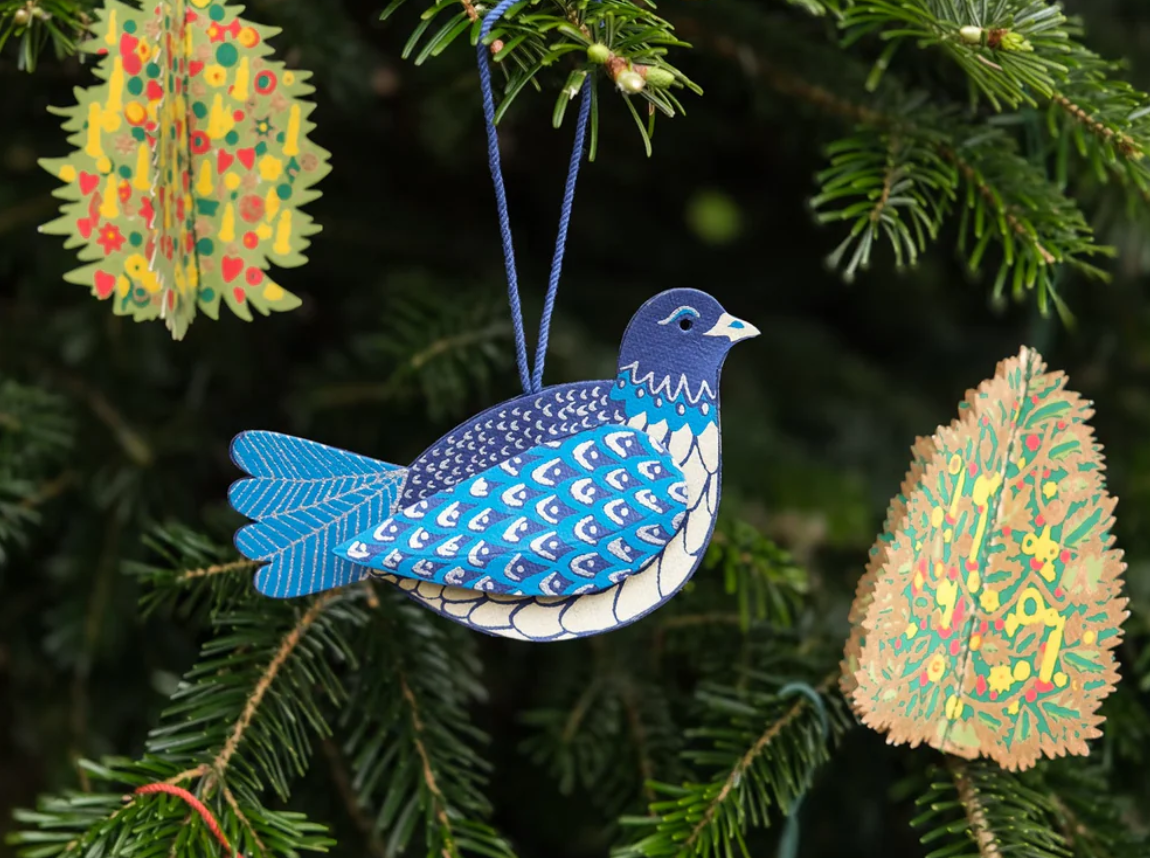 Decorative blue bird ornament hanging on a Christmas tree with other ornaments.