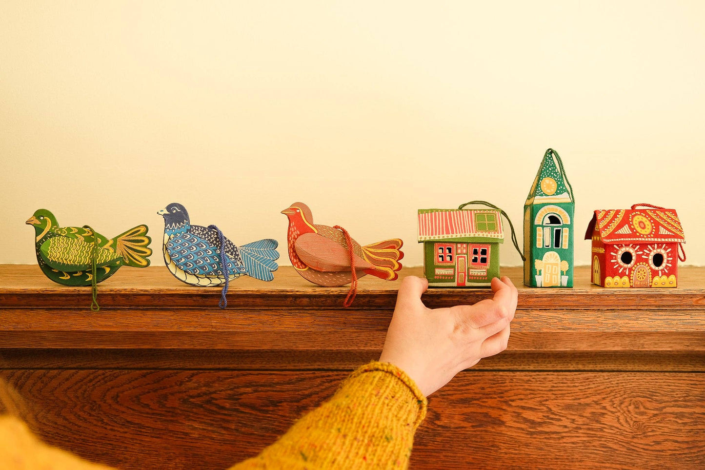Colorful birdhouses on a wooden shelf with a hand reaching out