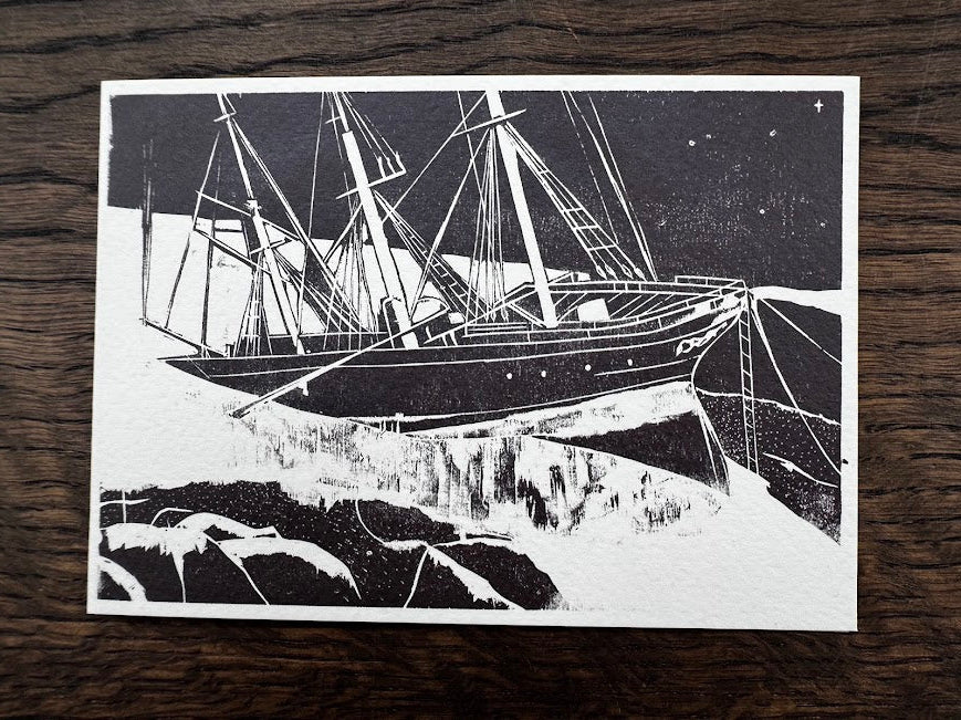 A black and white art print depicting a detailed ship's rigging and mast against a starry night sky, placed flat on a dark wood background.