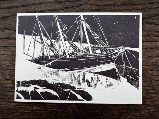 A black and white art print depicting a detailed ship's rigging and mast against a starry night sky, placed flat on a dark wood background.