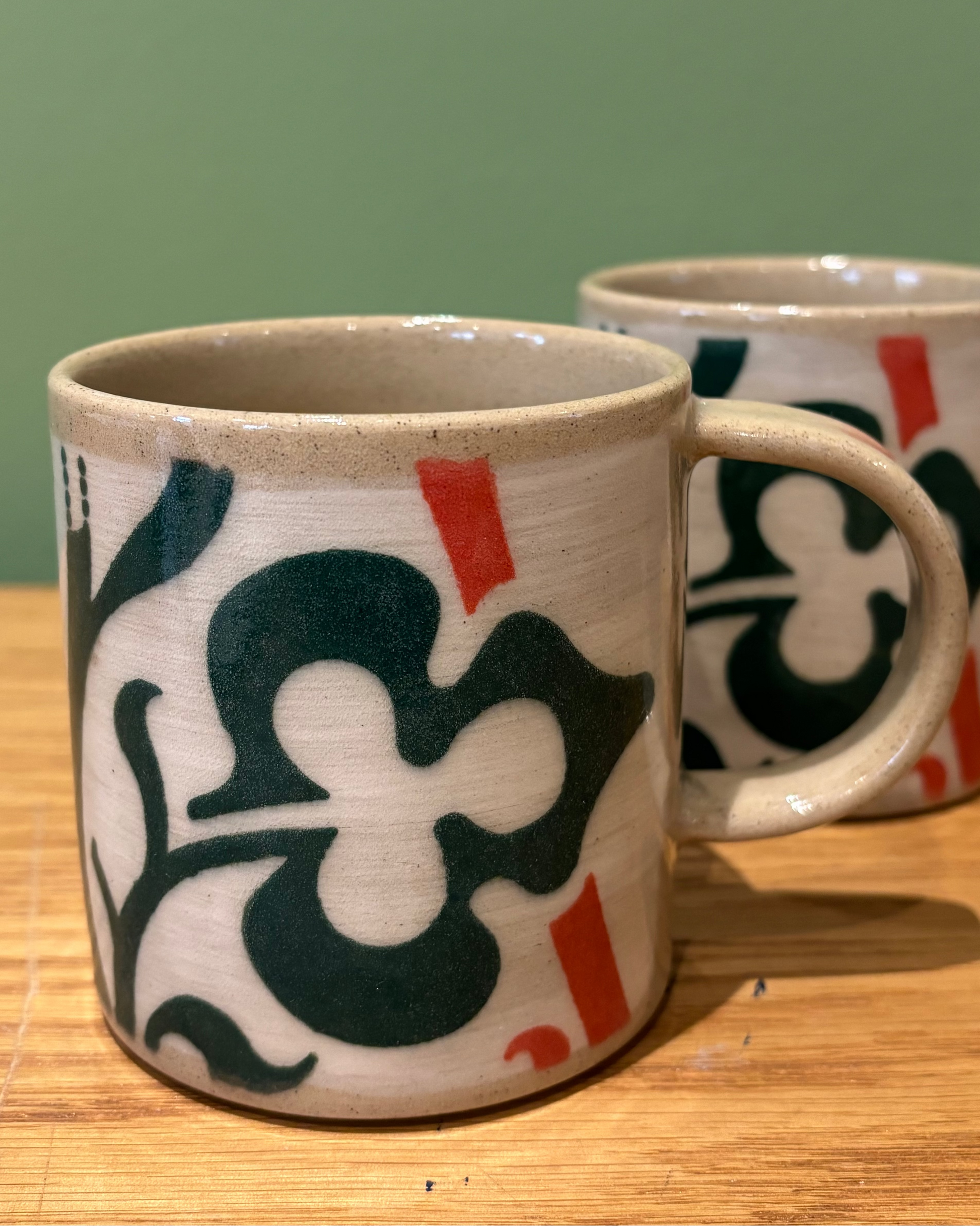 Two ceramic mugs with decorative patterns on a wooden surface and green background