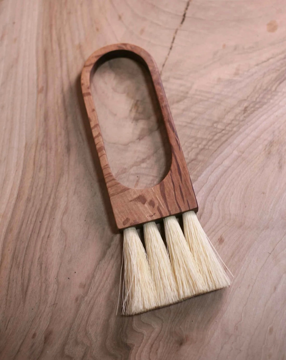 A handcrafted wooden brush with natural fiber bristles, laying on a wooden surface.