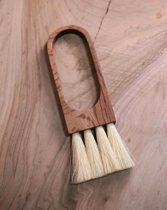 A handcrafted wooden brush with natural fiber bristles, laying on a wooden surface.