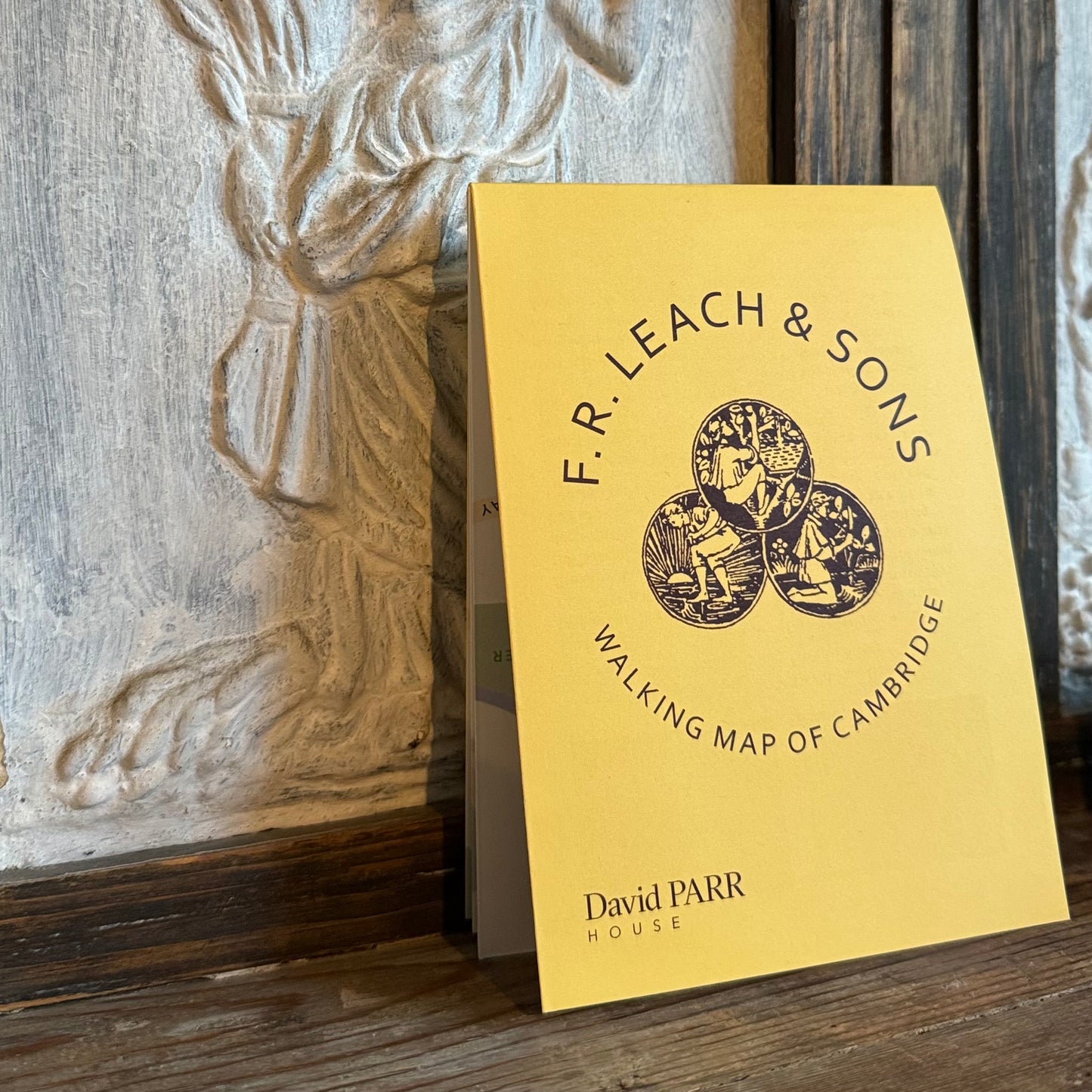 Yellow map of Cambridge by F.R. Leach & Sons on a wooden surface with decorative background