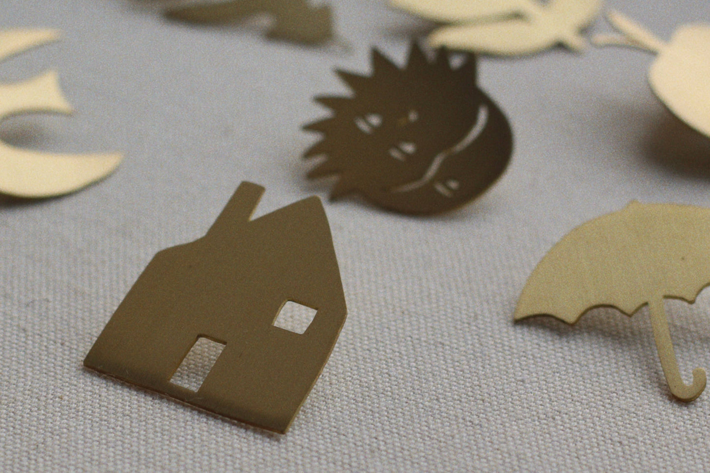 Cardboard cutouts of a house, hedgehog, and umbrella on a textured surface