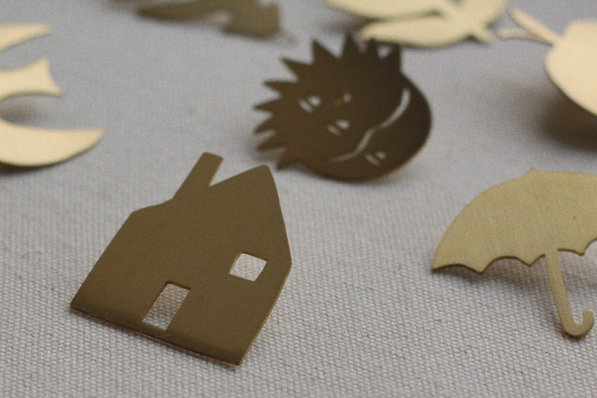 Cardboard cutouts of a house, hedgehog, and umbrella on a textured surface