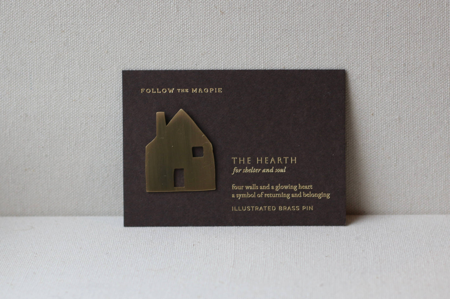 Decorative house-shaped brooch on a black card with text against a gray background