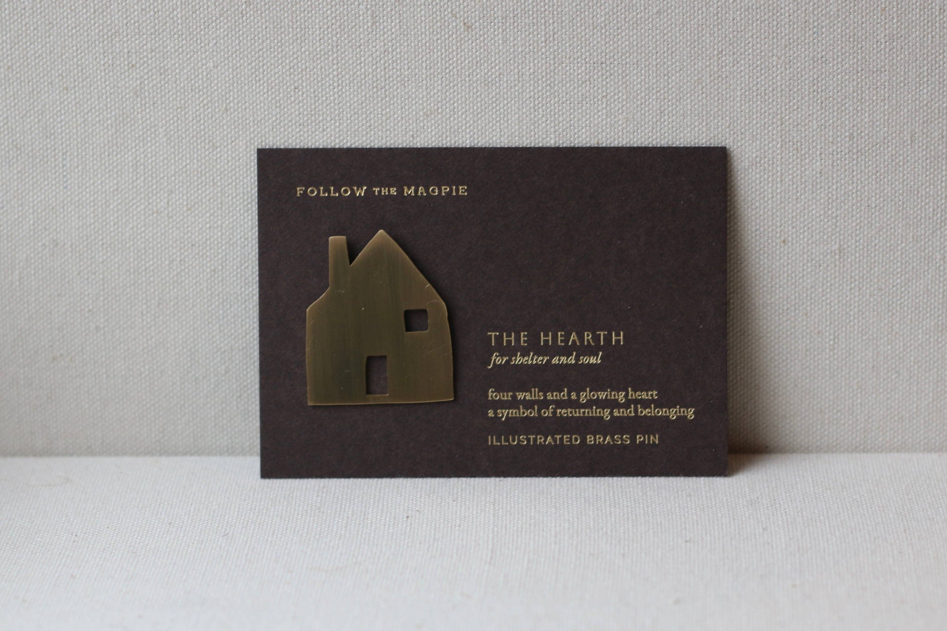 Decorative house-shaped brooch on a black card with text against a gray background