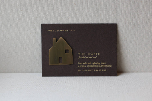 Decorative house-shaped brooch on a black card with text against a gray background