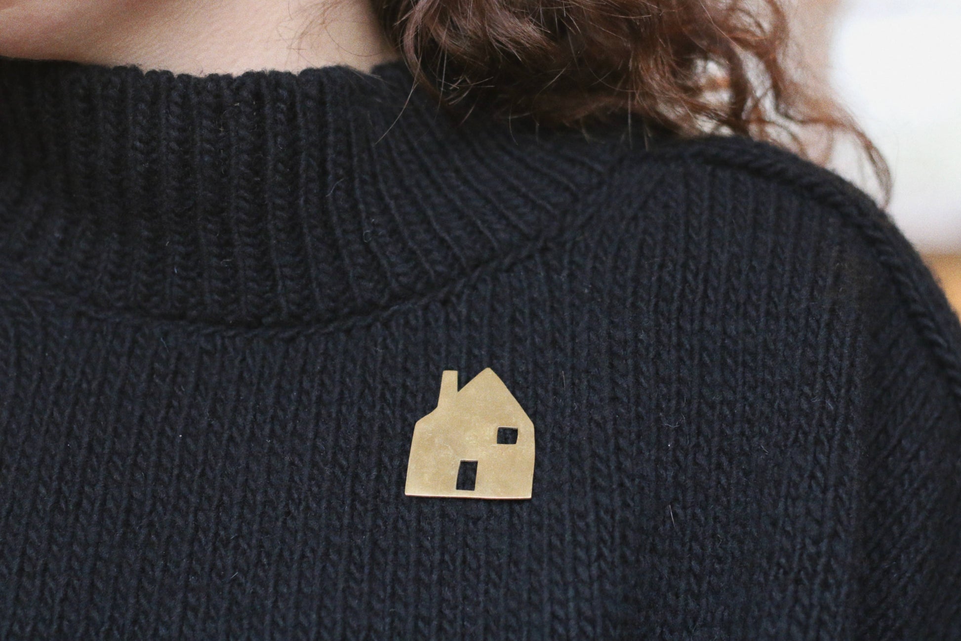 Black sweater with a gold house-shaped brooch worn by a person
