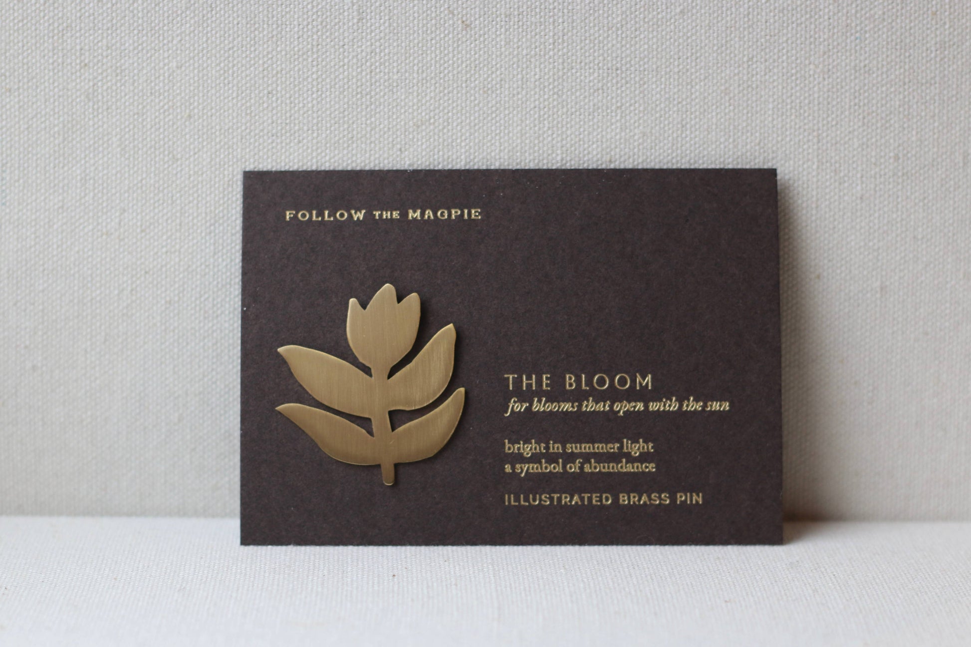 Brass flower-shaped pin on a black card with text against a gray background