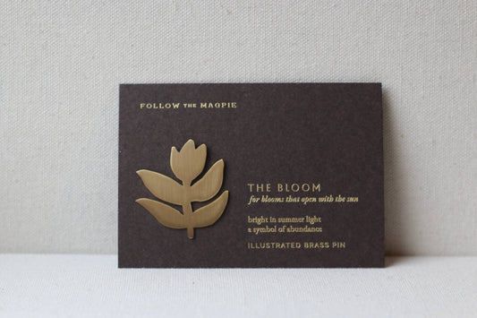 Brass flower-shaped pin on a black card with text against a gray background