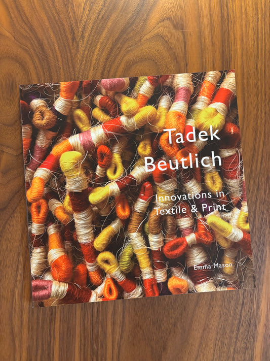 Book cover with colorful textile design and text on a wooden surface