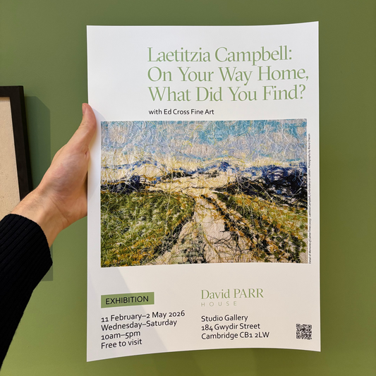 Hand holding a poster for an art exhibition titled 'Laetitia Campbell: On Your Way Home, What Did You Find?' against a green wall.